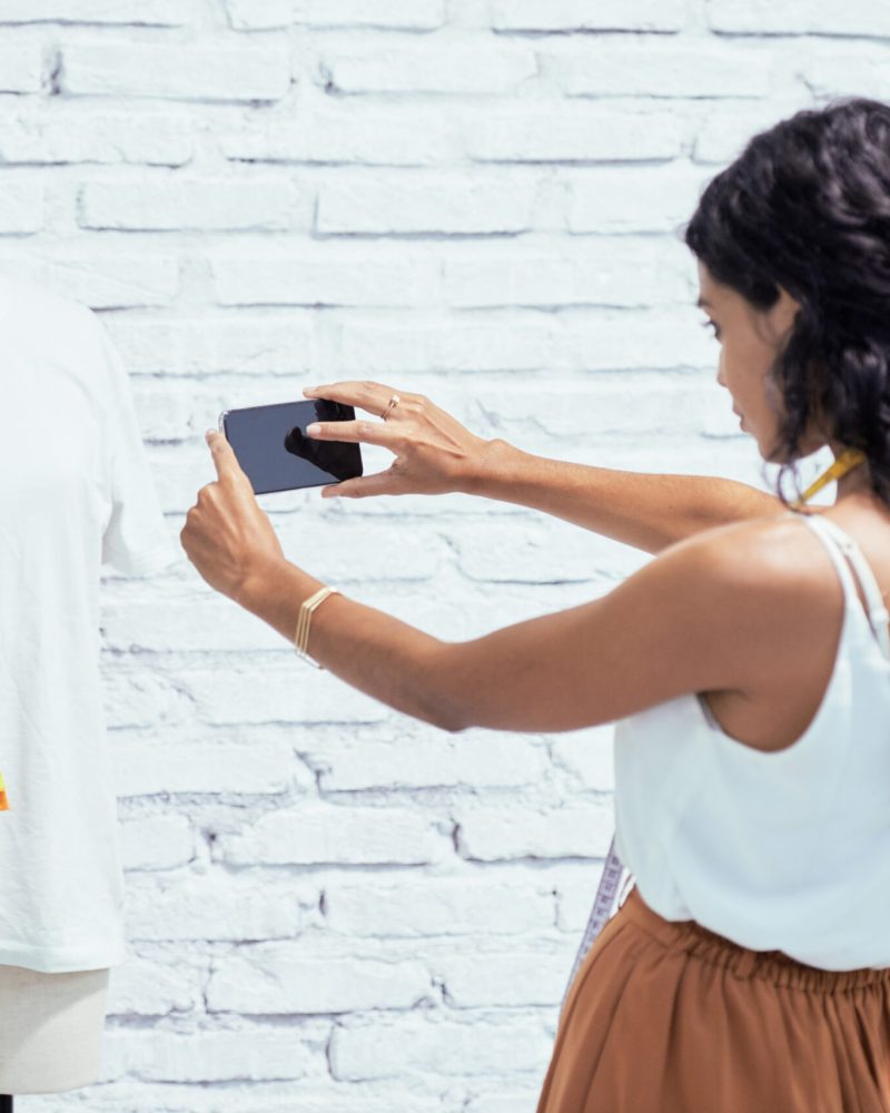 Young female designer photographing the mannequin with white shirt and colorful palette on her smartphone and sending it to the client